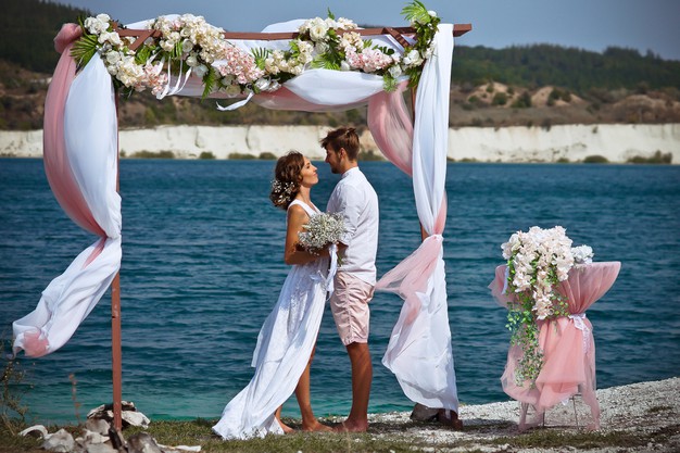novia novio vestidos blanco ramo flores blancas paran arco flores tela sobre fondo lago azul arena blanca 267226 221